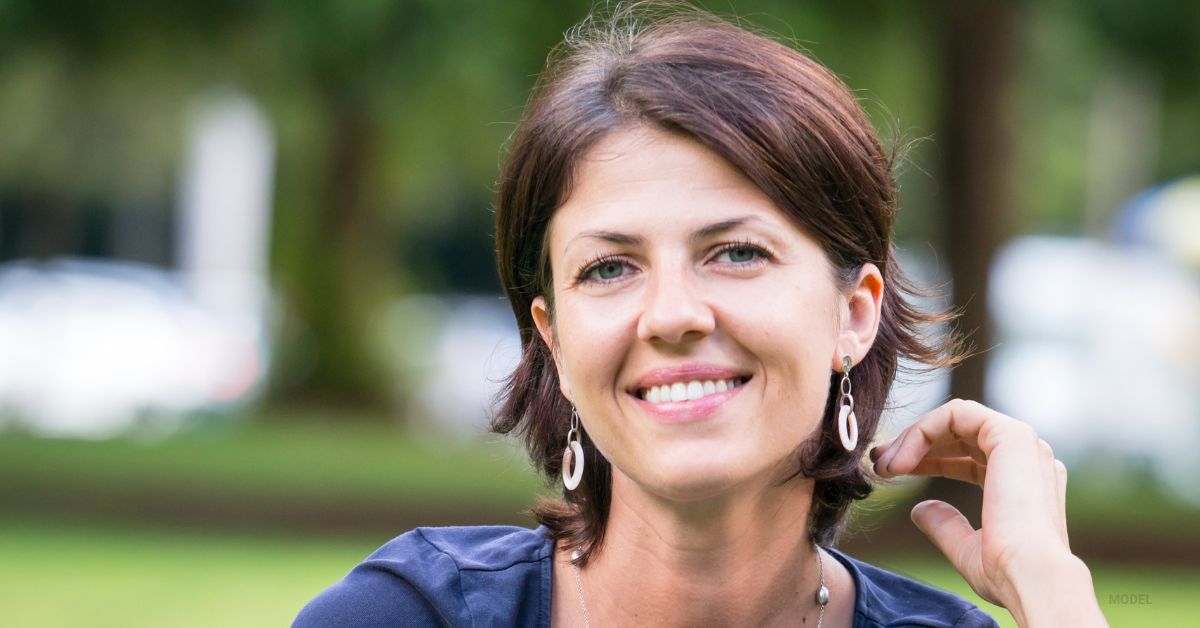 a female (model) in her early 40s smiling and enjoying being outdoors